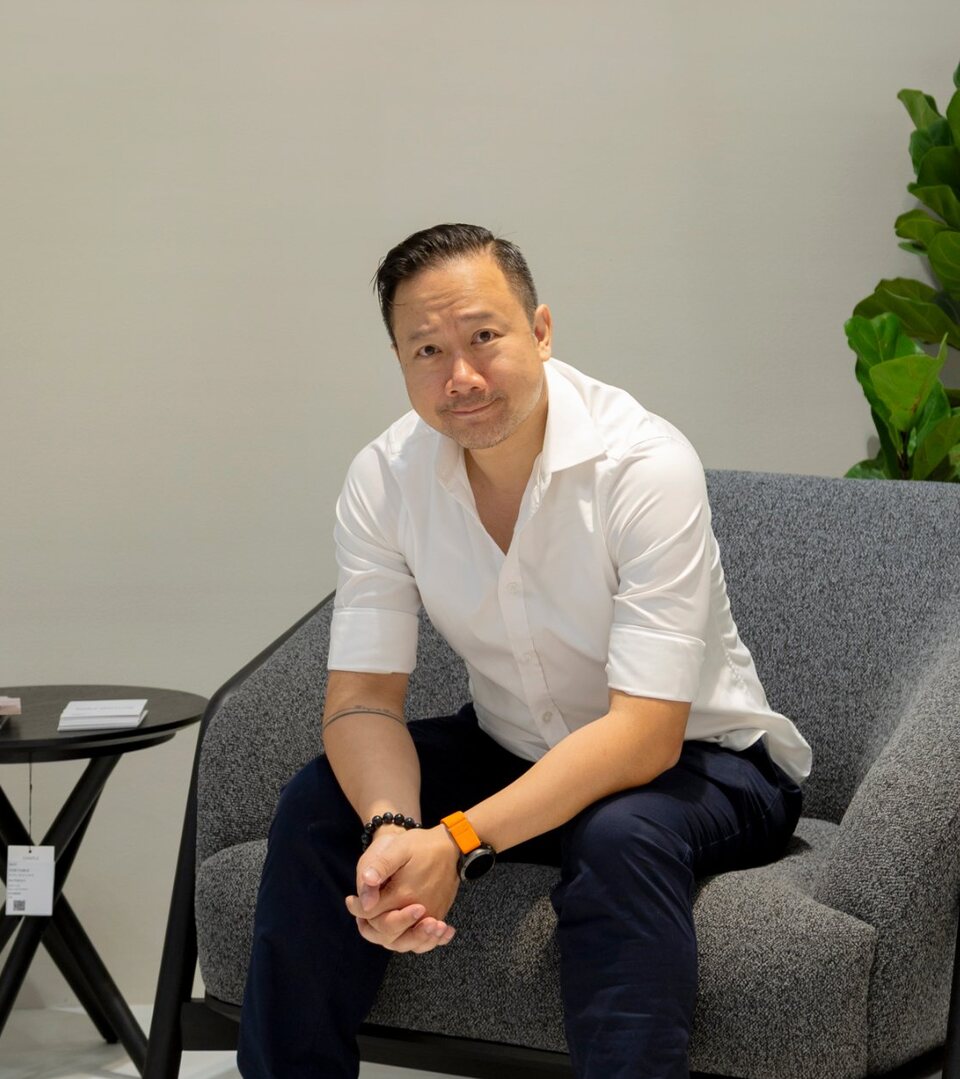 Portrait of Dino seated in a grey lounge chair in a furniture showroom
